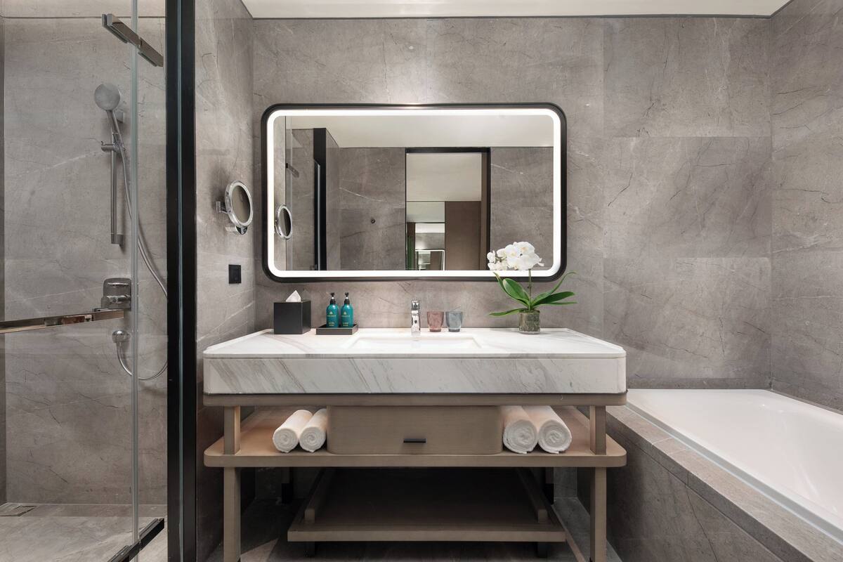 A modern bathroom with a large mirror, a bathtub, and a shower area.