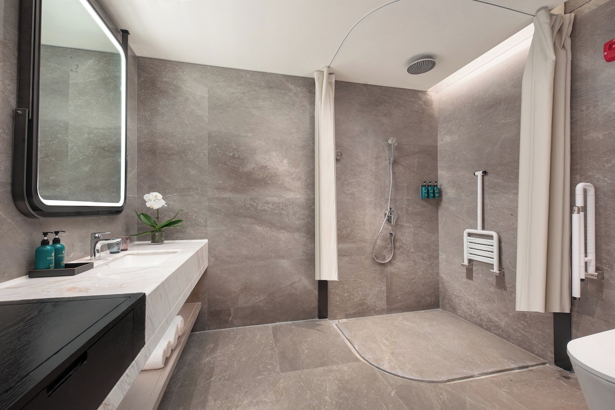 A modern bathroom with a large mirror, a shower, and a toilet.