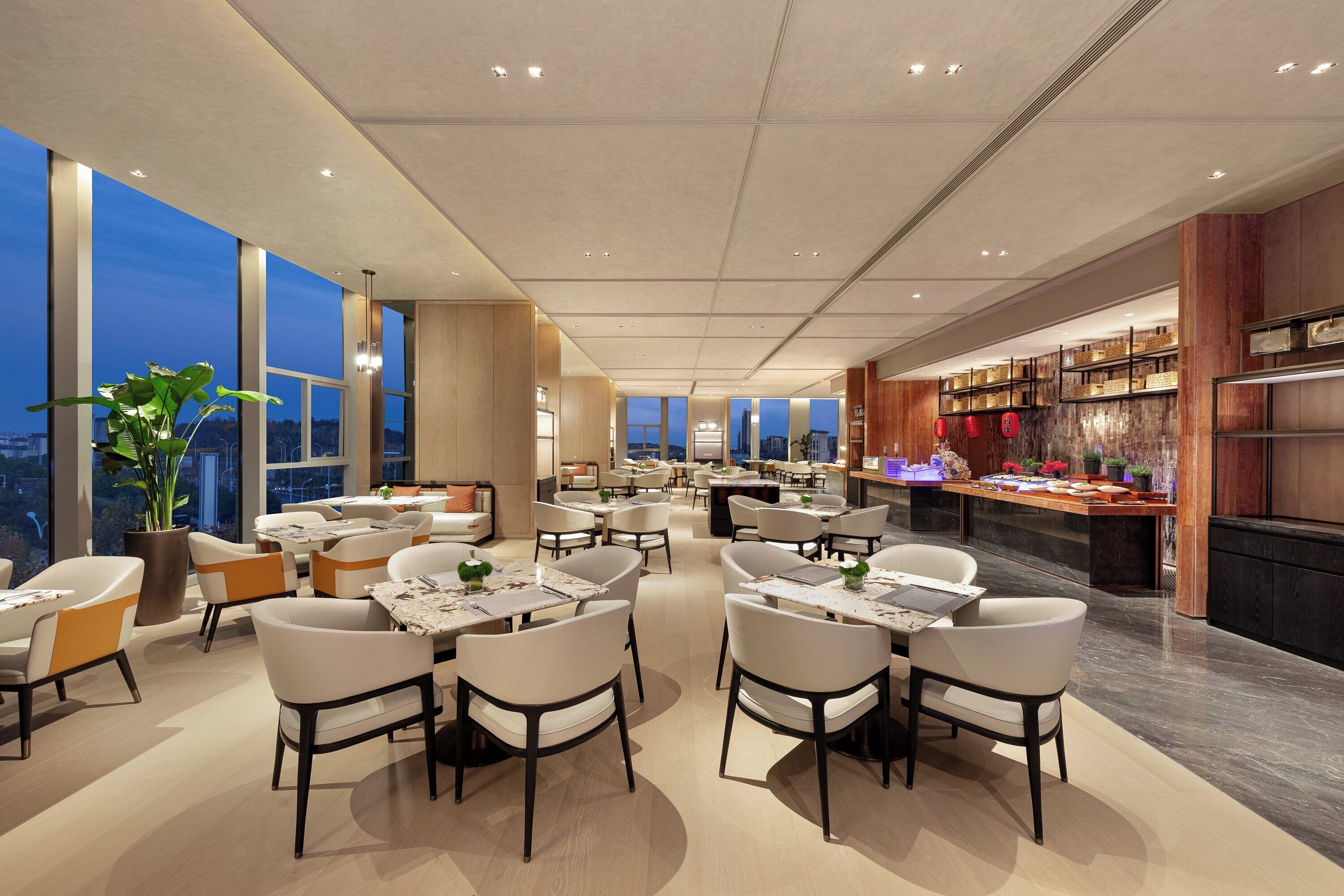A modern dining area with high ceilings, large windows, and a variety of seating arrangements.