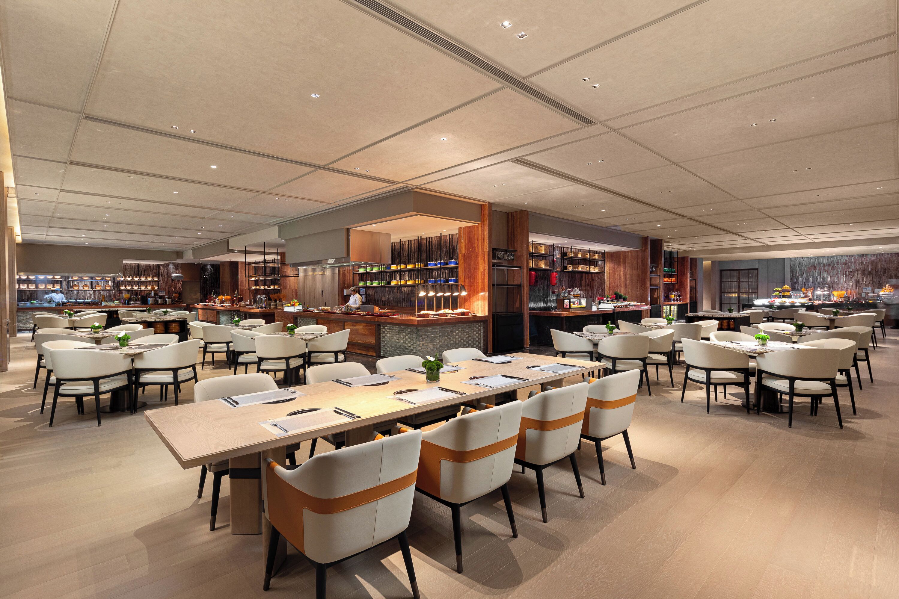A spacious restaurant with multiple dining tables and chairs, a bar area, and a view of the cityscape.