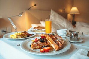 A breakfast setting with waffles, strawberries, and a glass of orange juice on a table.