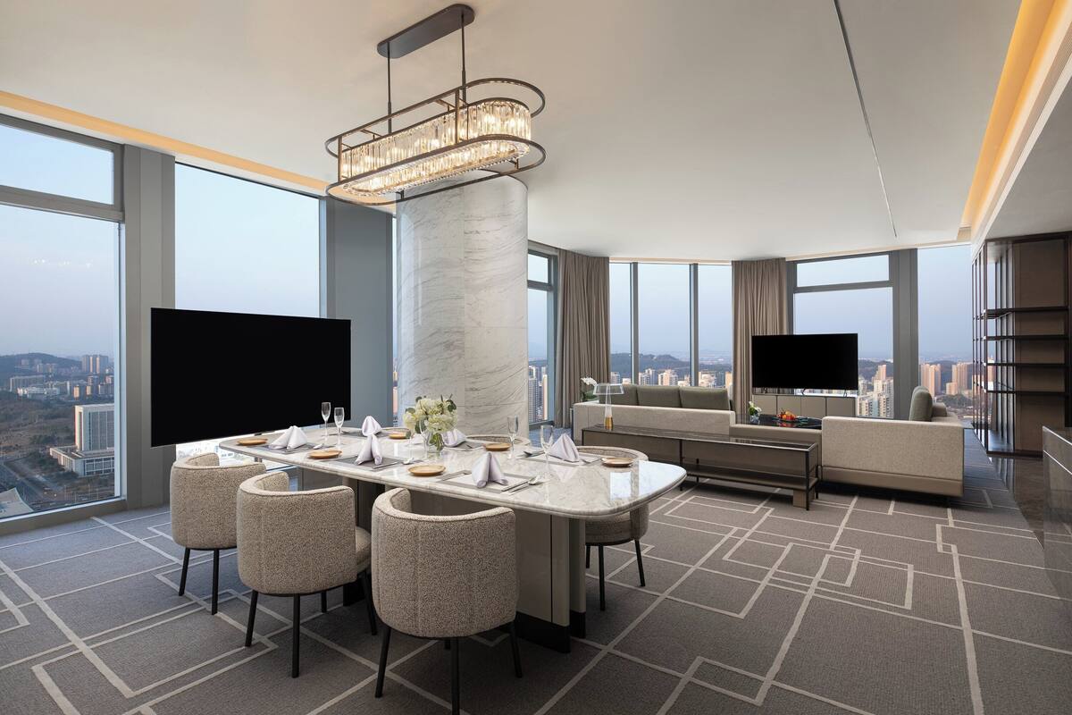 A modern hotel room with a dining area, a sofa, and a TV.