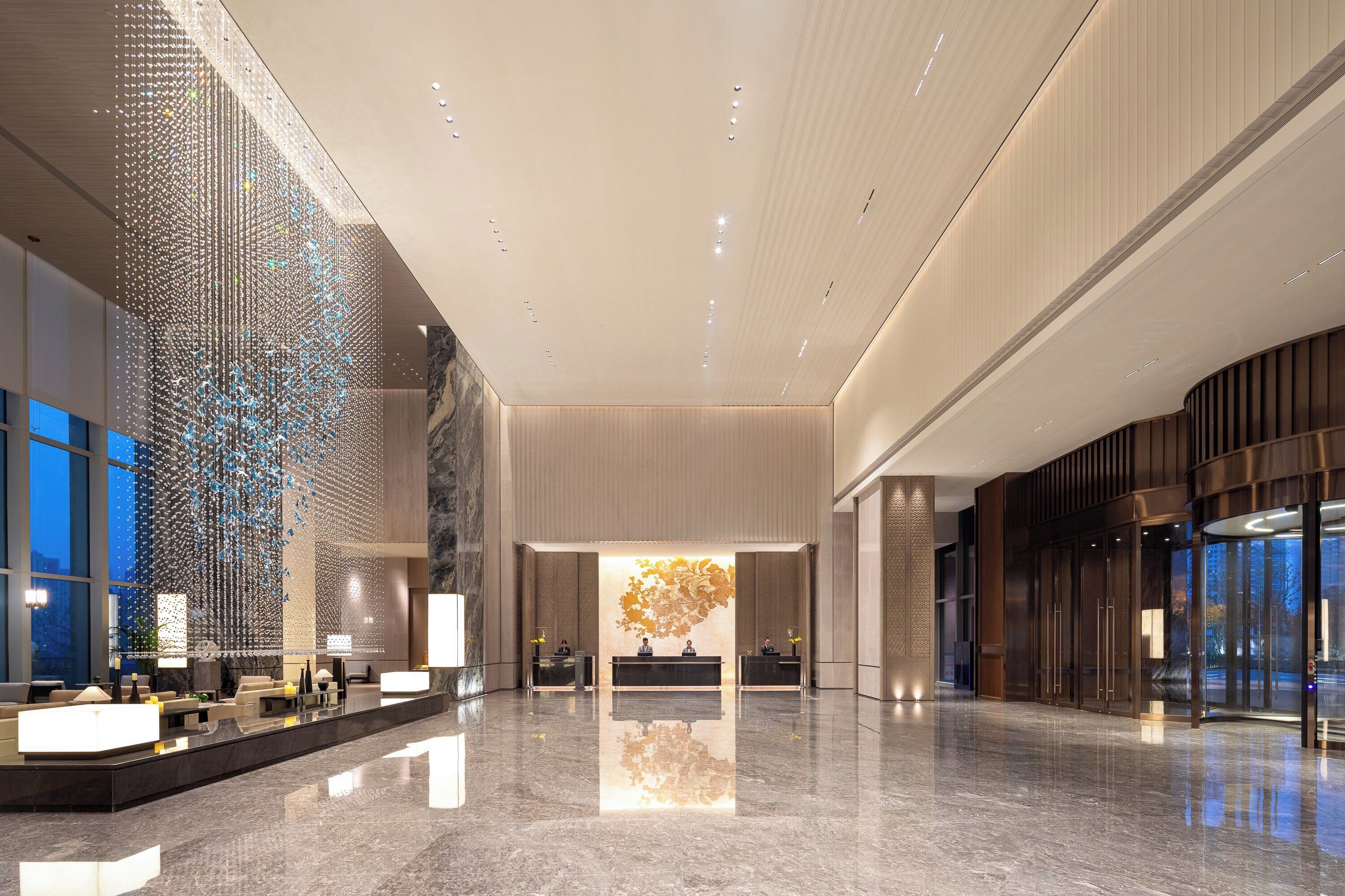 Een ruime lobby met een spiegelende vloer, een receptiebalie en een decoratieve lichtinstallatie.