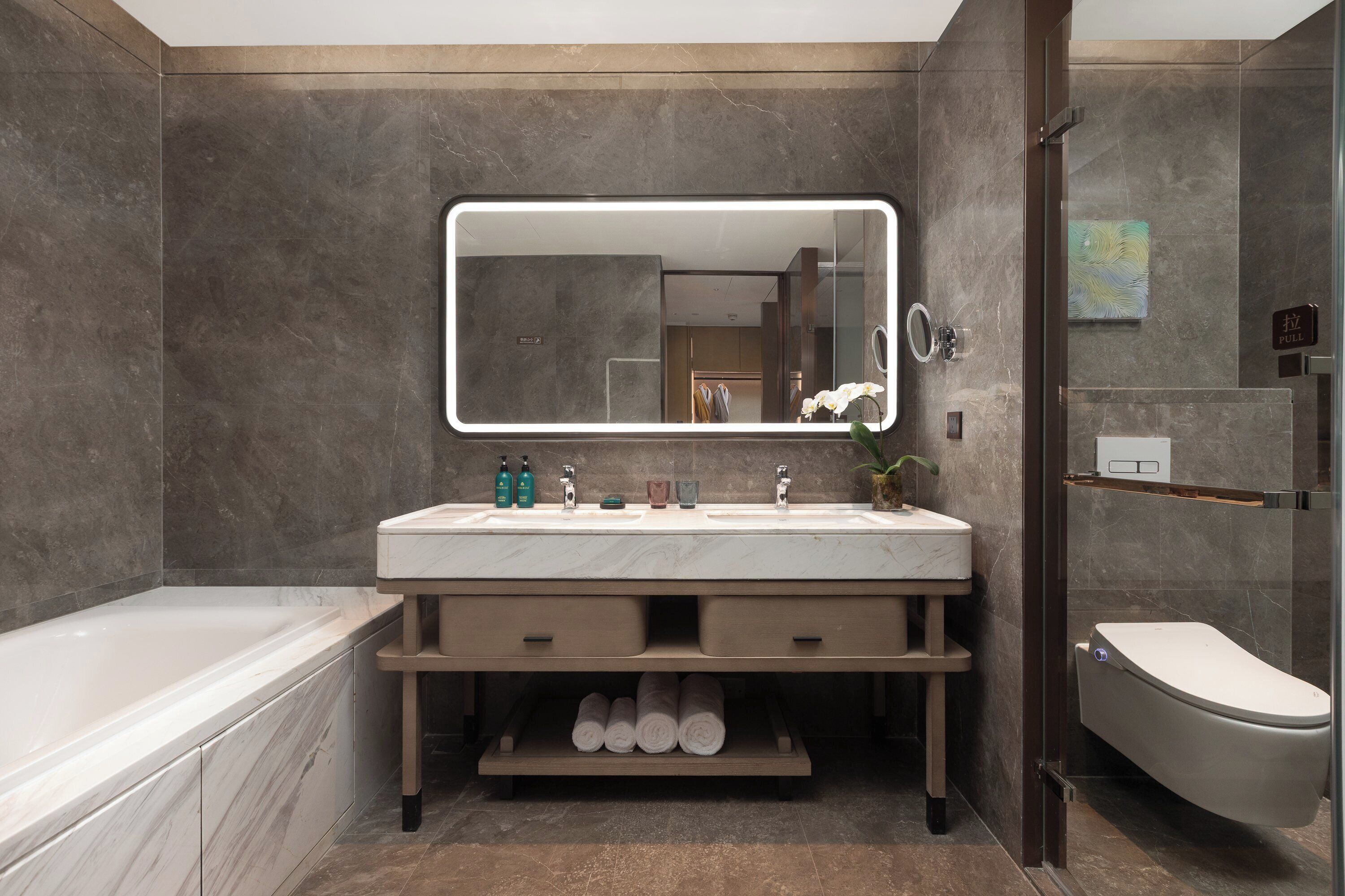 Un baño moderno con un espejo grande, lavamanos dobles, una bañera y un inodoro.