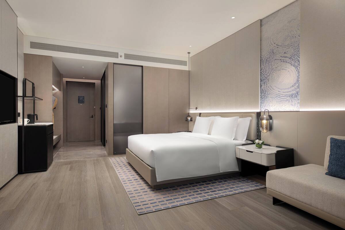 A modern hotel room with a large bed, bedside tables, a desk, and a TV.