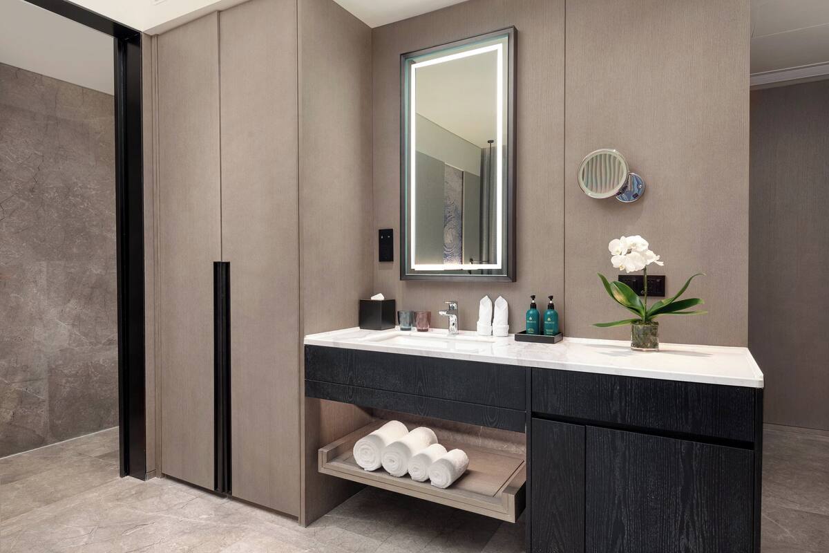 A modern bathroom with a large mirror, a sink, and a shelf with towels.