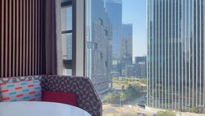 Una camera d'hotel moderna con un'ampia finestra che si affaccia su alti palazzi e sullo skyline della città.