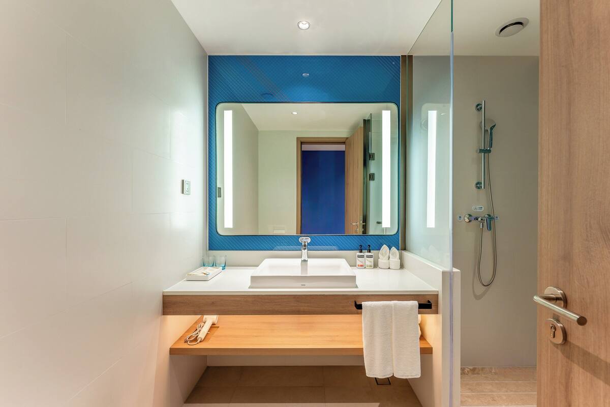 Un baño moderno con un espejo grande, un lavabo, una ducha y un banco de madera.