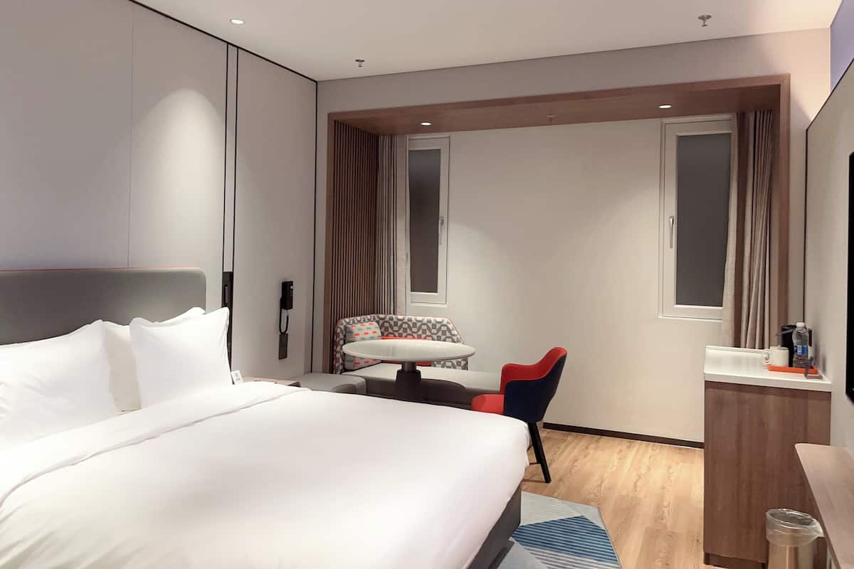 Habitación de hotel con una cama grande, un escritorio con silla, una ventana y una pequeña mesa con otra silla.