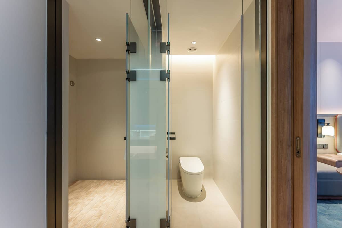 Un baño moderno con cabina de ducha de vidrio, inodoro blanco y piso de madera.