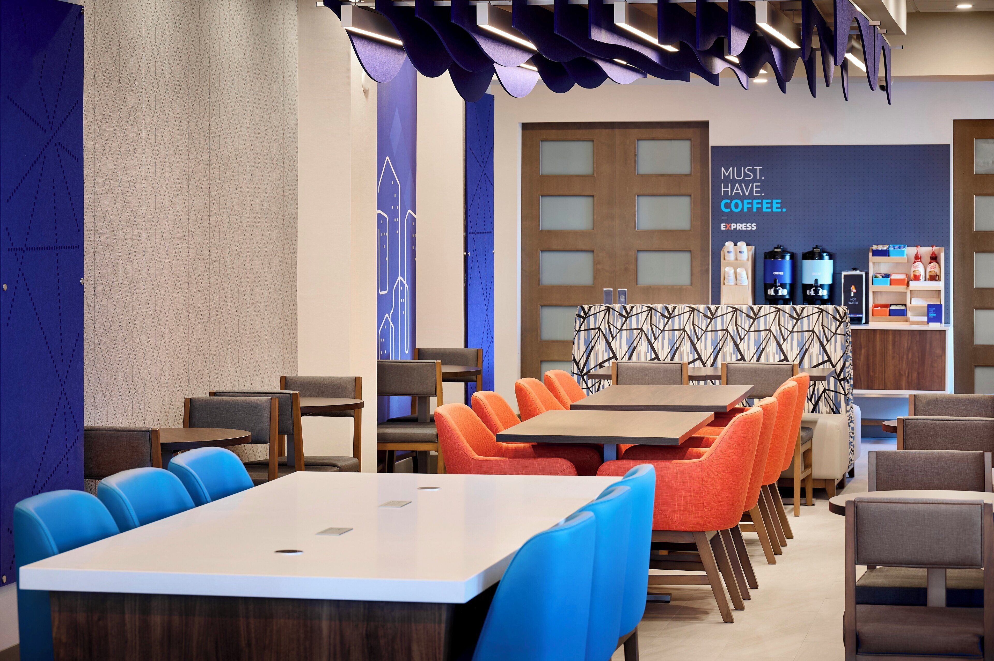 A modern coffee shop with a seating area featuring tables and chairs, a counter with coffee machines, and a wall with a coffee advertisement.