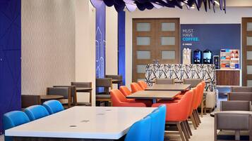A modern coffee shop with a seating area featuring tables and chairs, a counter with coffee machines, and a wall with a coffee advertisement.