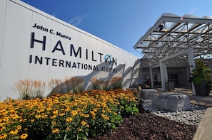 The exterior of John C. Munro Hamilton International Airport with a large sign, a covered entrance, and a landscaped area with yellow flowers.