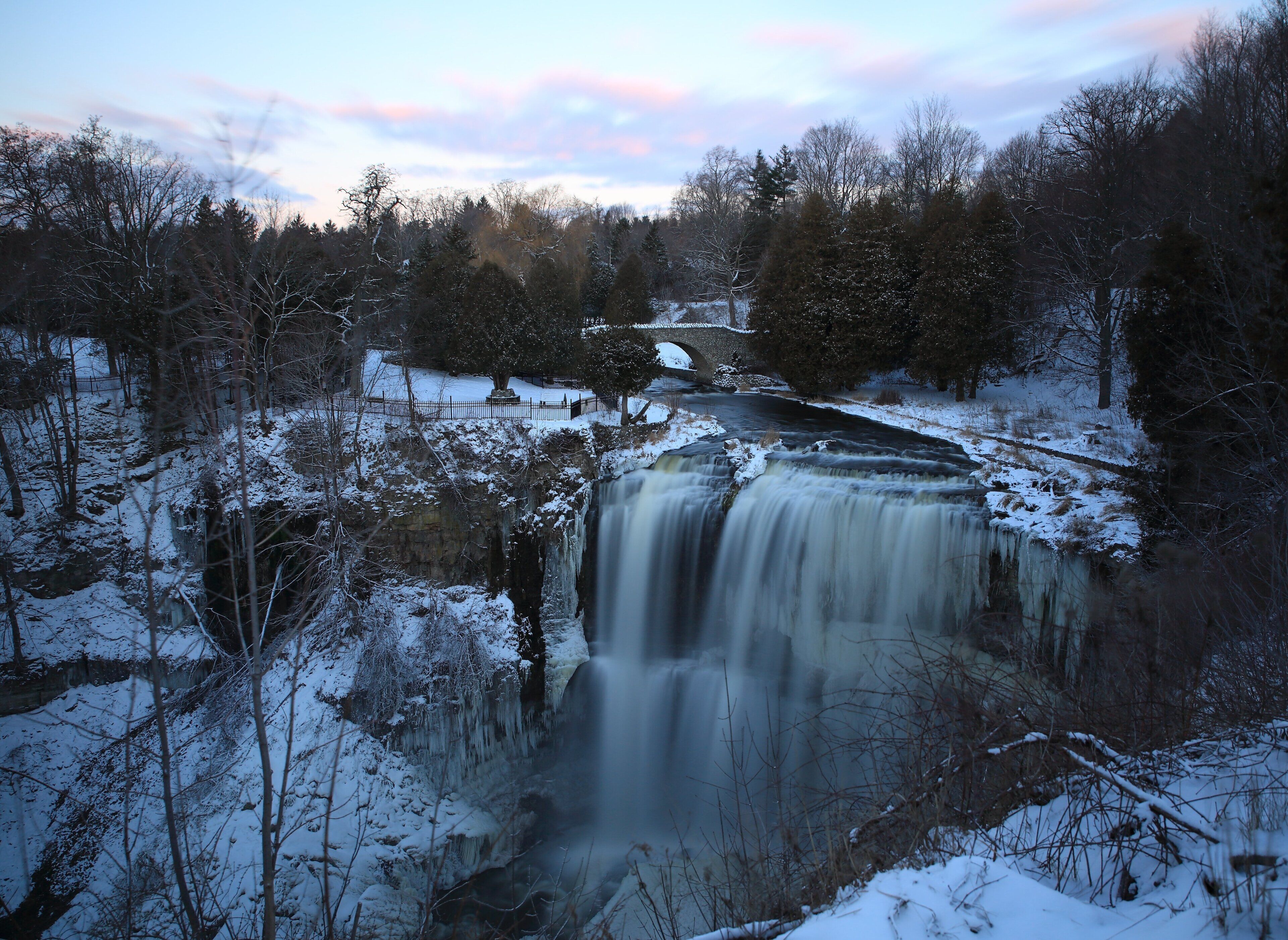 A waterfall surrounded by snow-covered trees and a stone bridge.