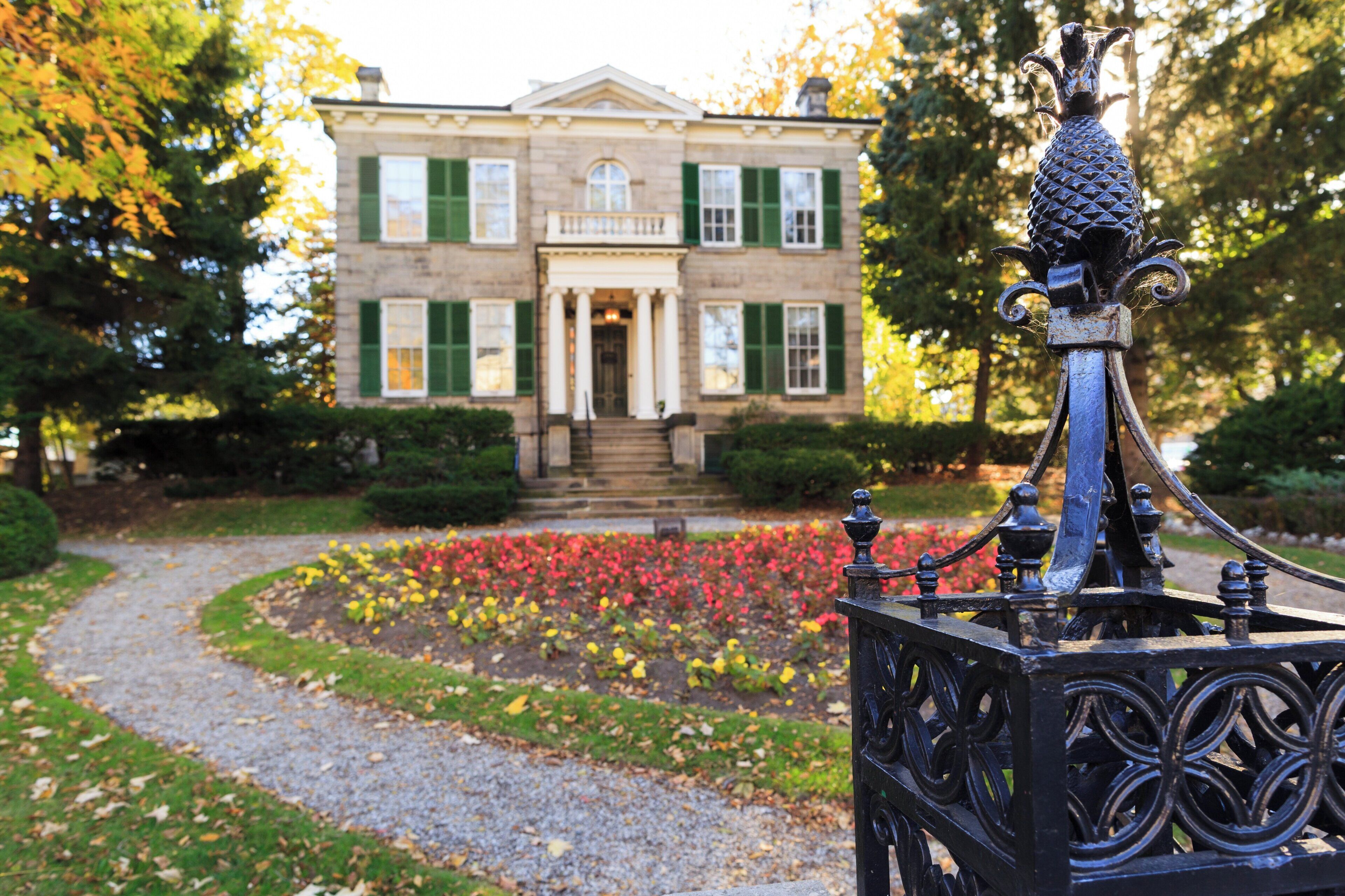 A historic building with a symmetrical facade, a central entrance with columns, and a well-maintained garden with colorful flowers.