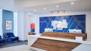 A modern reception desk with a blue and white color scheme, a framed artwork on the wall, and a blue chair to the left.
