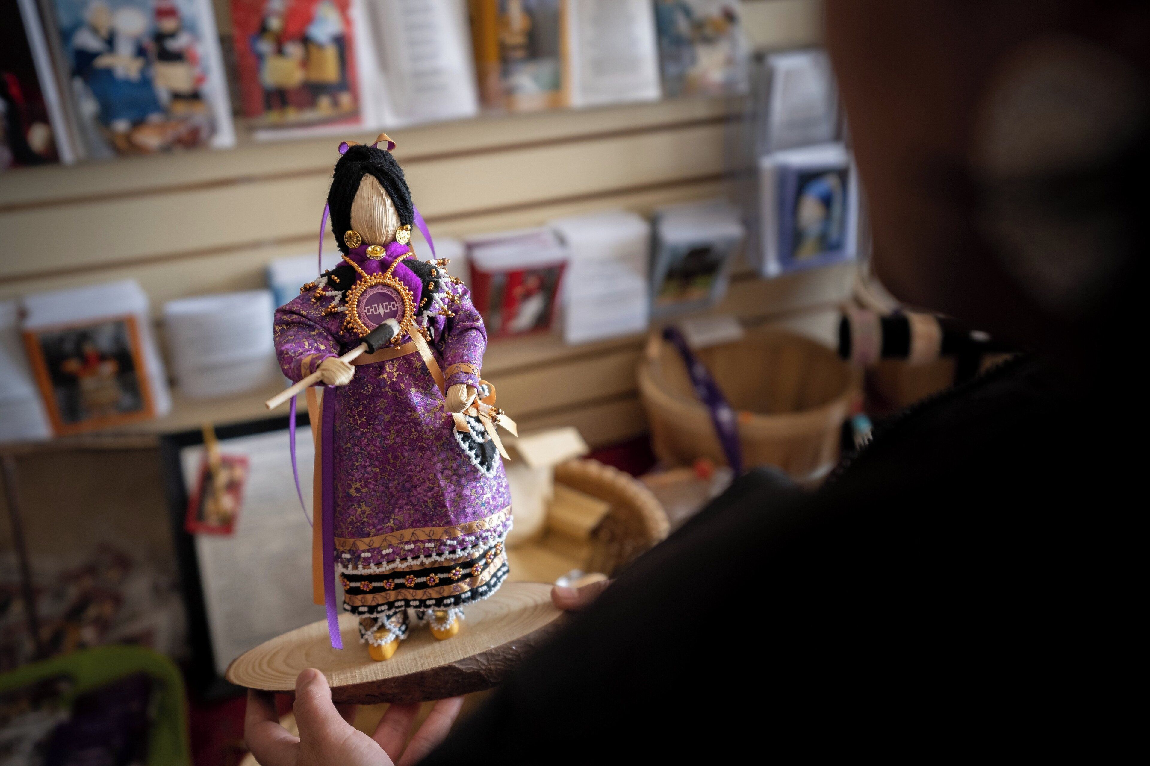 Una persona sosteniendo una muñeca vestida con un traje morado con detalles dorados.