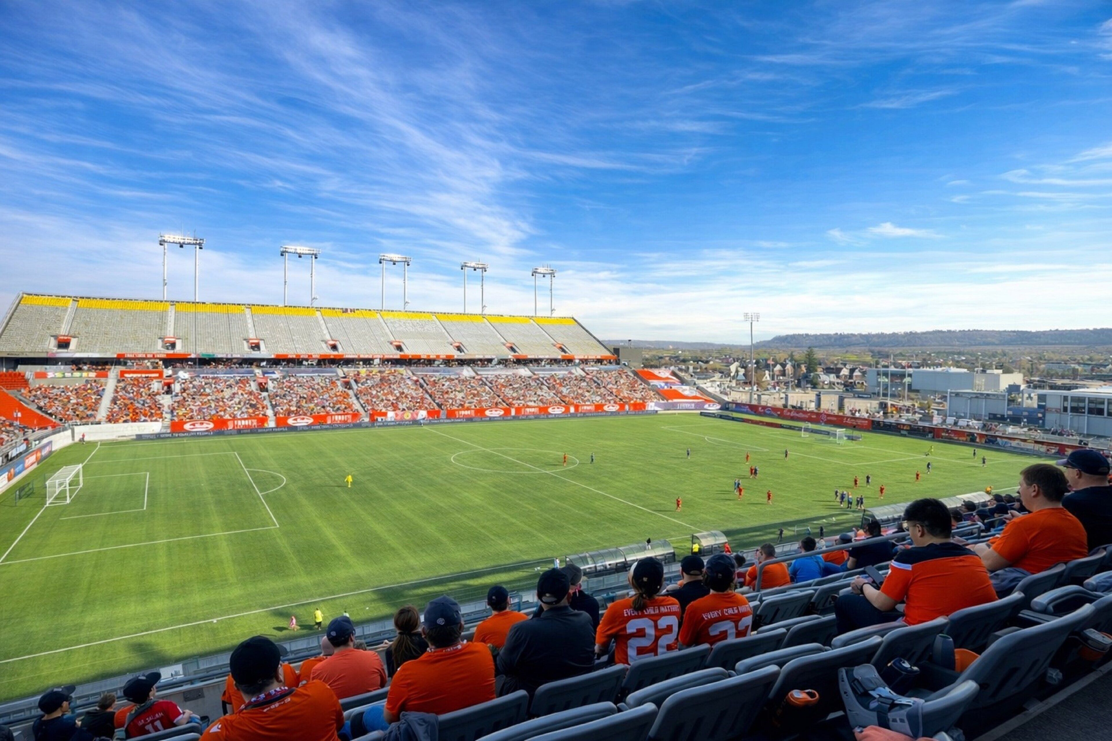 Een stadion met tribunes, een voetbalveld en een heldere lucht.