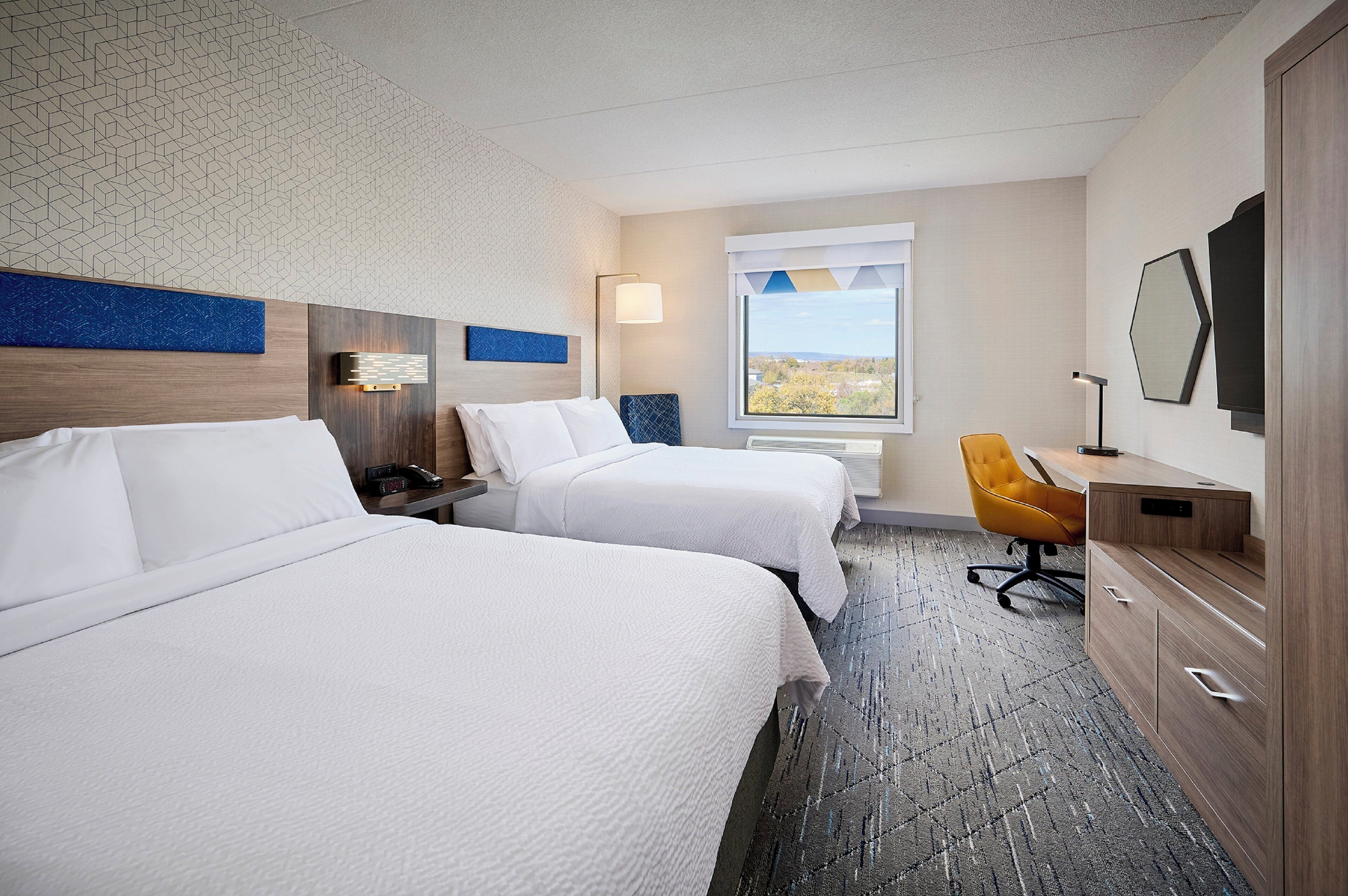 Een hotelkamer met twee bedden, een bureau, een stoel en een raam met uitzicht.