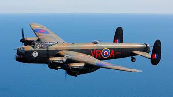 A vintage military aircraft in flight over a body of water.