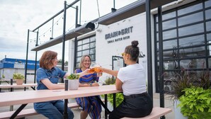 Three people seated at an outdoor table with a building labeled "GRAIN & GRIT" in the background. - Holiday Inn Express Hamilton Upper James by IHG (Hamilton)
