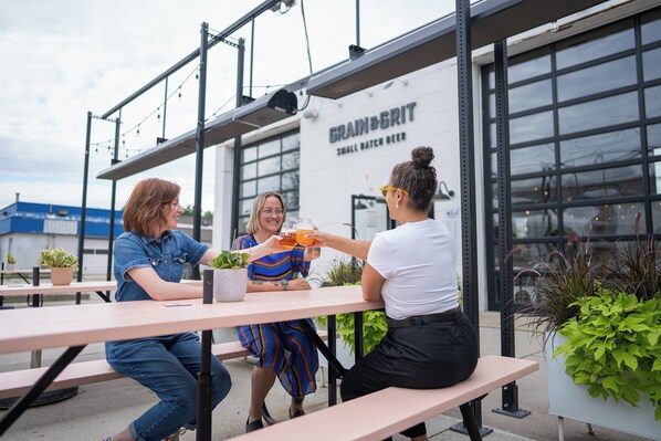 Trois personnes sont assises à une table à l’extérieur, et on aperçoit en arrière-plan un bâtiment sur lequel on peut lire l’inscription « GRAIN & GRIT ».
