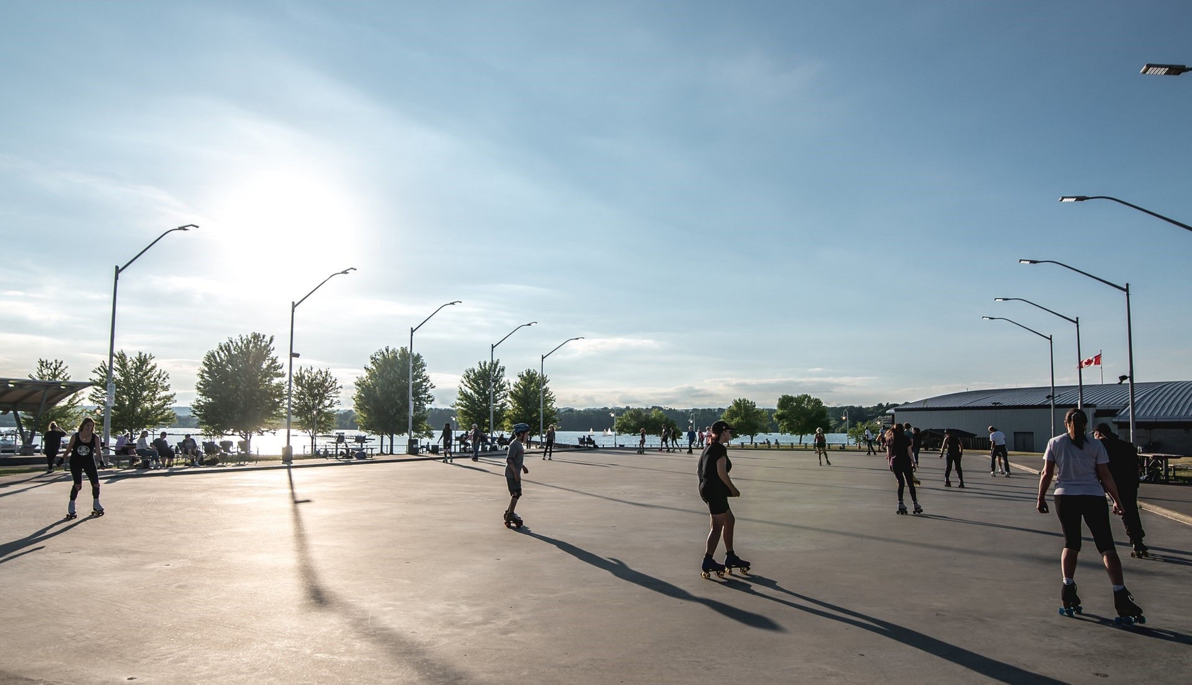 An outdoor skating rink with people skating, surrounded by trees and a body of water in the background.