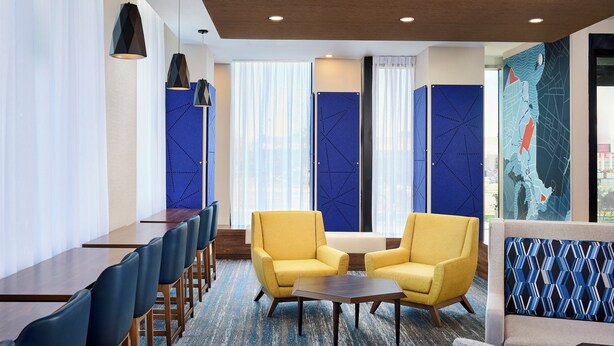 Een hotellobby met een lange receptiebalie, twee gele fauteuils, een klein tafeltje en een blauwe wand met een patroon.