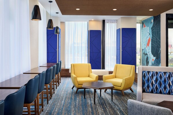 A hotel lobby with a long reception desk, two yellow armchairs, a small table, and a blue patterned wall. - Holiday Inn Express Hamilton Upper James by IHG (Hamilton)