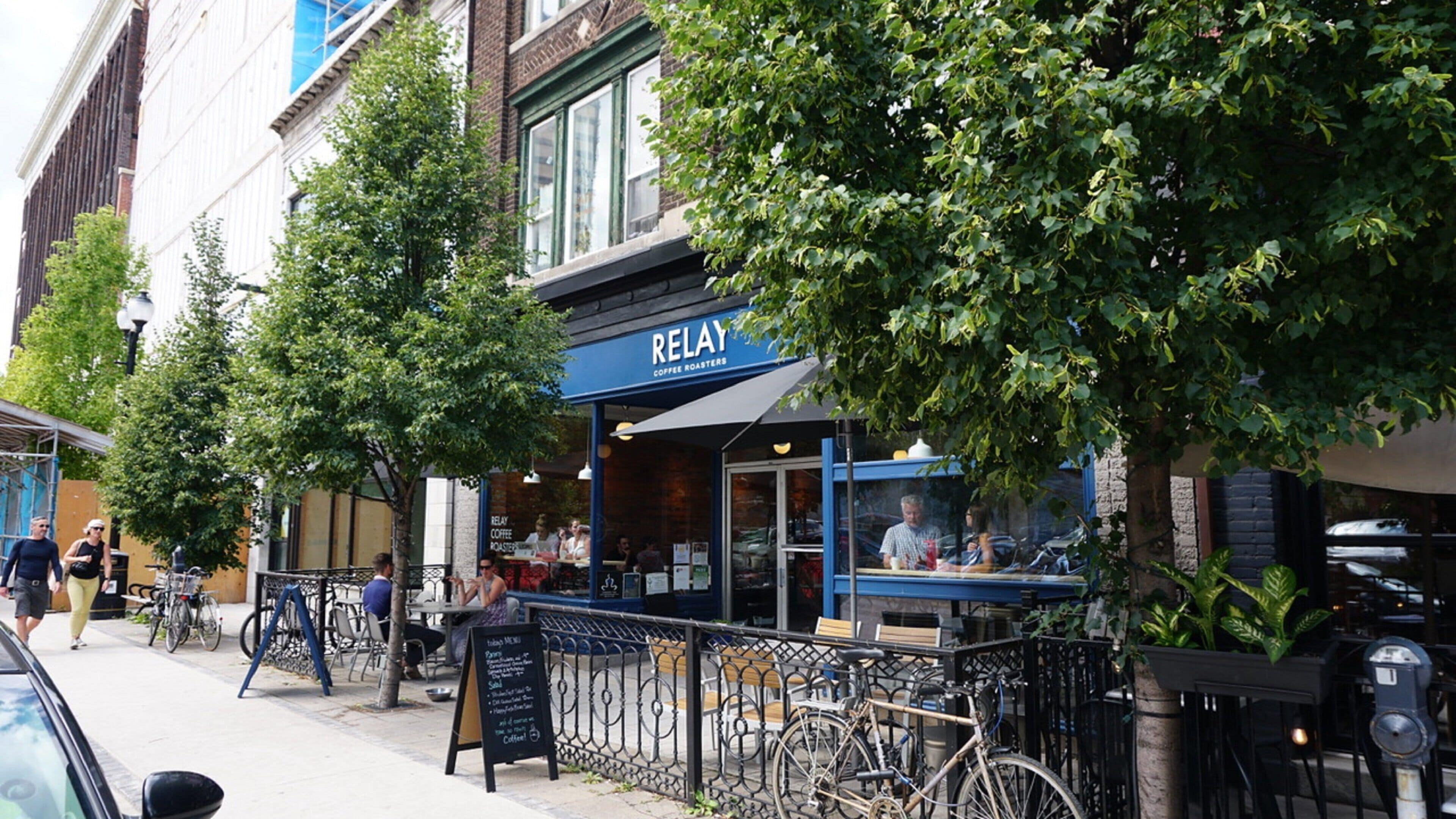 Calle con terraza al aire libre frente a una torrefactora de café llamada 'RELAY', bicicletas estacionadas y acera.