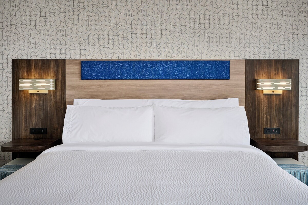 A hotel room with a large bed, two nightstands, a blue accent wall, and wall-mounted lamps.