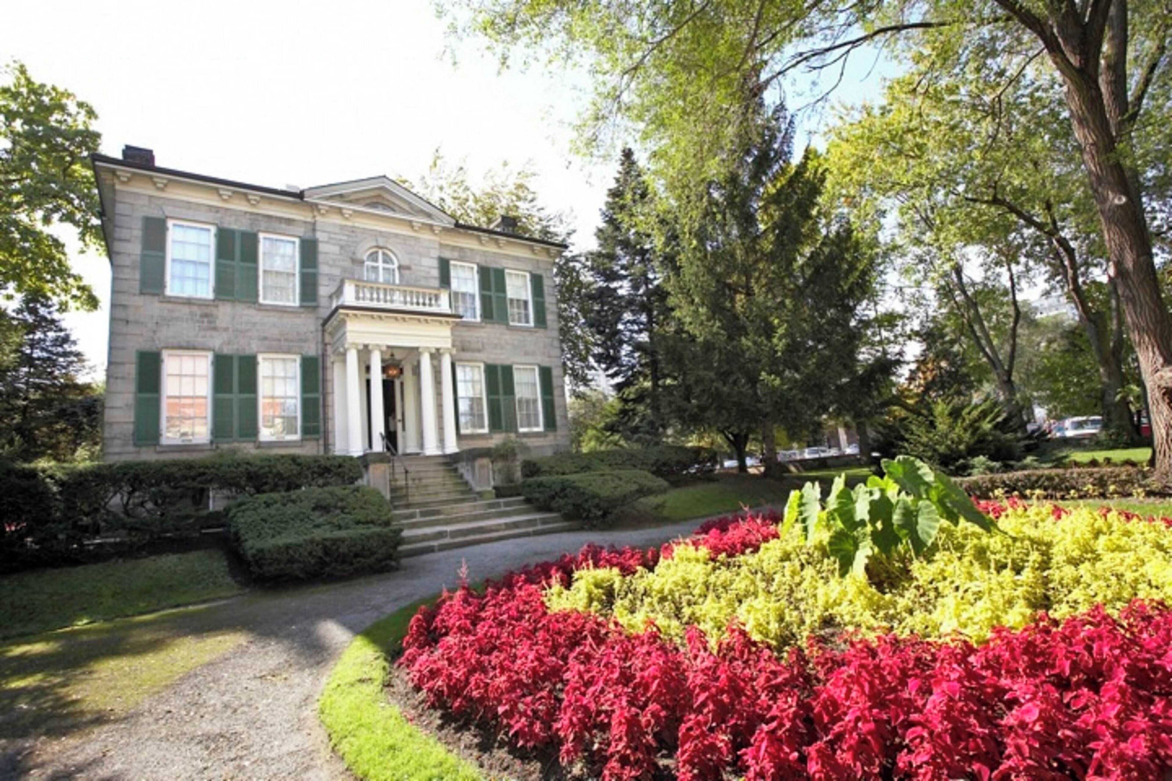 A two-story building with a symmetrical facade, a central entrance with columns, and a well-manicured garden with red and yellow foliage.