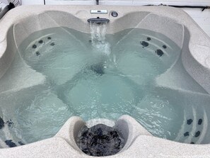 A hot tub with a waterfall feature, a control panel, and multiple seating areas.
