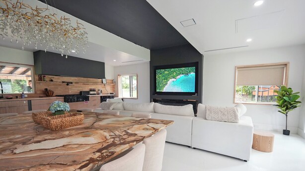 Una sala de estar moderna con un gran comedor de madera, un sofá blanco y un televisor de pantalla plana montado en la pared.