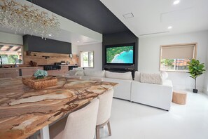 Un salon moderne avec une grande table à manger en bois, un canapé blanc et un téléviseur à écran plat fixé au mur.
