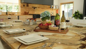 Una cocina bien iluminada con encimera de mármol, una mesa de comedor de madera dispuesta con platos, cubiertos y una botella de vino.
