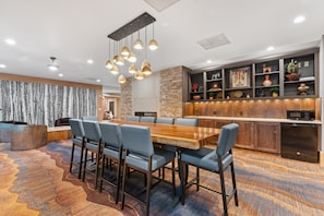 A modern dining area with a wooden table and blue chairs, a kitchen with a stone wall, and a decorative shelf with various items. - Sm8194-3 (Keystone)