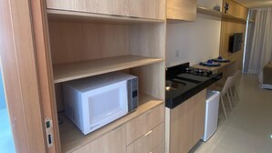 A modern kitchen with wooden cabinets, a microwave, a stove, and a small refrigerator. - Villas do Porto - 111 by La Playa (Ipojuca)