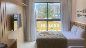 A hotel room with a bed, a desk, a TV, and a view of the outside. - Villas do Porto - 111 by La Playa (Ipojuca)