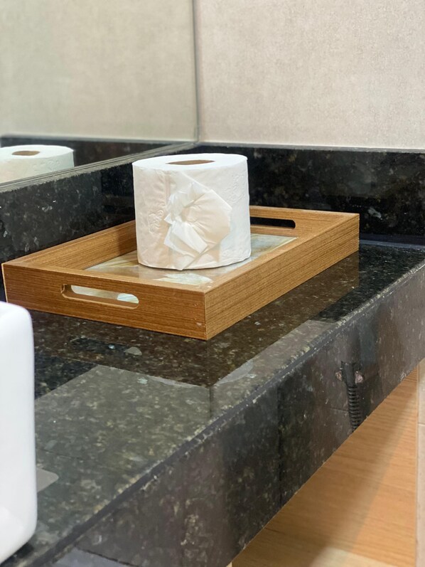 A wooden tray with a roll of toilet paper on a black marble countertop. - Villas do Porto - 111 by La Playa (Ipojuca)