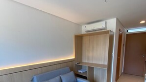 A modern living room with a grey sofa, wooden shelving, and an air conditioning unit. - Villas do Porto - 111 by La Playa (Ipojuca)