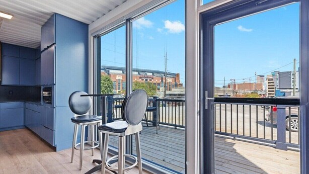 A modern kitchen with blue cabinets and a large sliding glass door leading to a balcony with a view of a stadium and cityscape. - Location Location Location! New Indy Custom Home (Indianapolis)