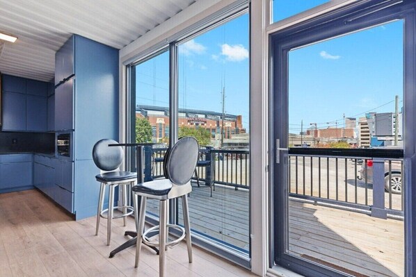 A modern kitchen with blue cabinets and a large sliding glass door leading to a balcony with a view of a stadium and cityscape.