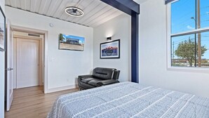 A bedroom with a bed, a black leather chair, a framed picture on the wall, and a window with a view of buildings and trees. - Location Location Location! New Indy Custom Home (Indianapolis)