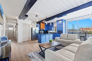A modern living room with a sofa, coffee table, and a kitchen area with blue cabinets and a central island. - Location Location Location! New Indy Custom Home (Indianapolis)