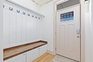 A hallway with a white coat rack, a wooden bench, and a door with a window. - Location Location Location! New Indy Custom Home (Indianapolis)