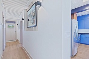 A hallway with a white door, a framed picture on the wall, and a kitchen area with blue cabinets and a white refrigerator.