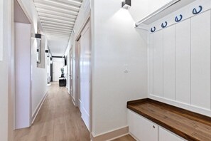 A hallway with white walls, wooden flooring, and a wooden counter with a sink.