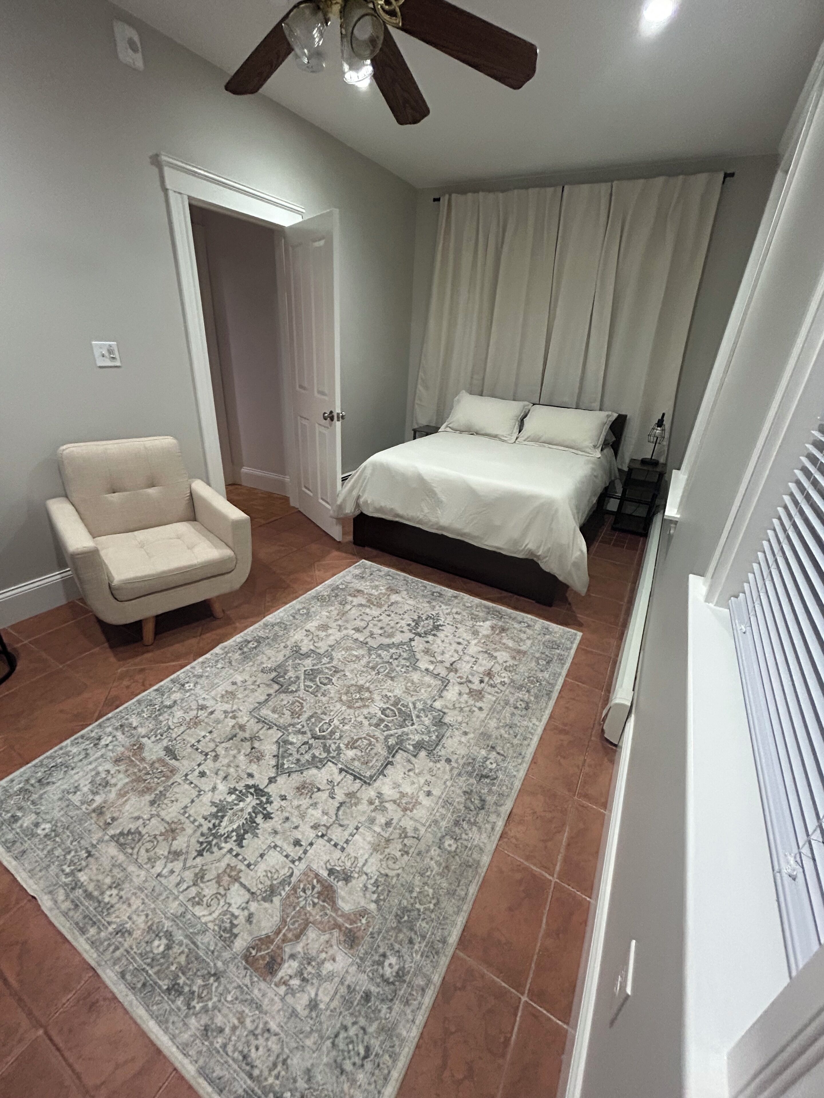 Une chambre à coucher avec un lit, une chaise, un ventilateur de plafond et un tapis à motifs.