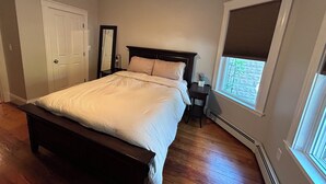 A bedroom with a bed, a nightstand, a mirror, a window with blinds, and a ceiling fan. - Harvard, B.U. M.I.T. Fenway Park convenient comfortable & spacious 3BR apartment (Cambridge)
